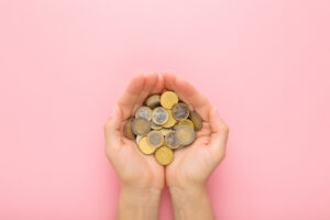 Opened young adult woman palms with euro coins on light pink table background. Pastel color. Point of view shot. Closeup. Top down view.