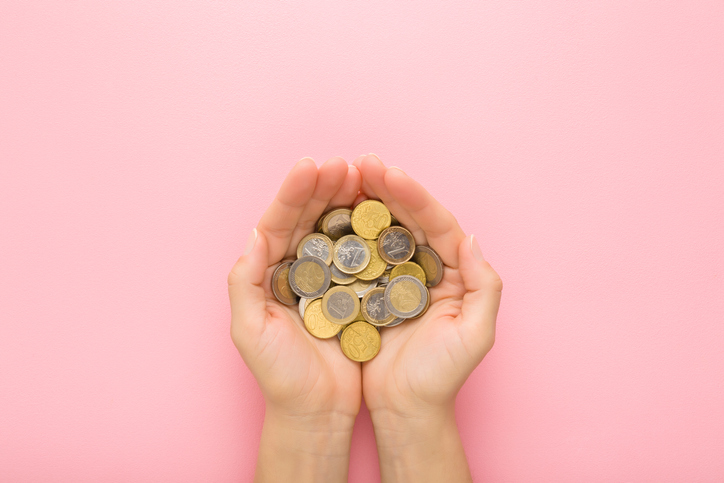 Opened young adult woman palms with euro coins on light pink table background. Pastel color. Point of view shot. Closeup. Top down view.